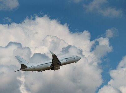 Ein Flugzeug hebt hoch in den Himmel ab, umgeben von weißen Wolken. Der Himmel ist blau und klar, was die Flugbewegung des Jets betont.