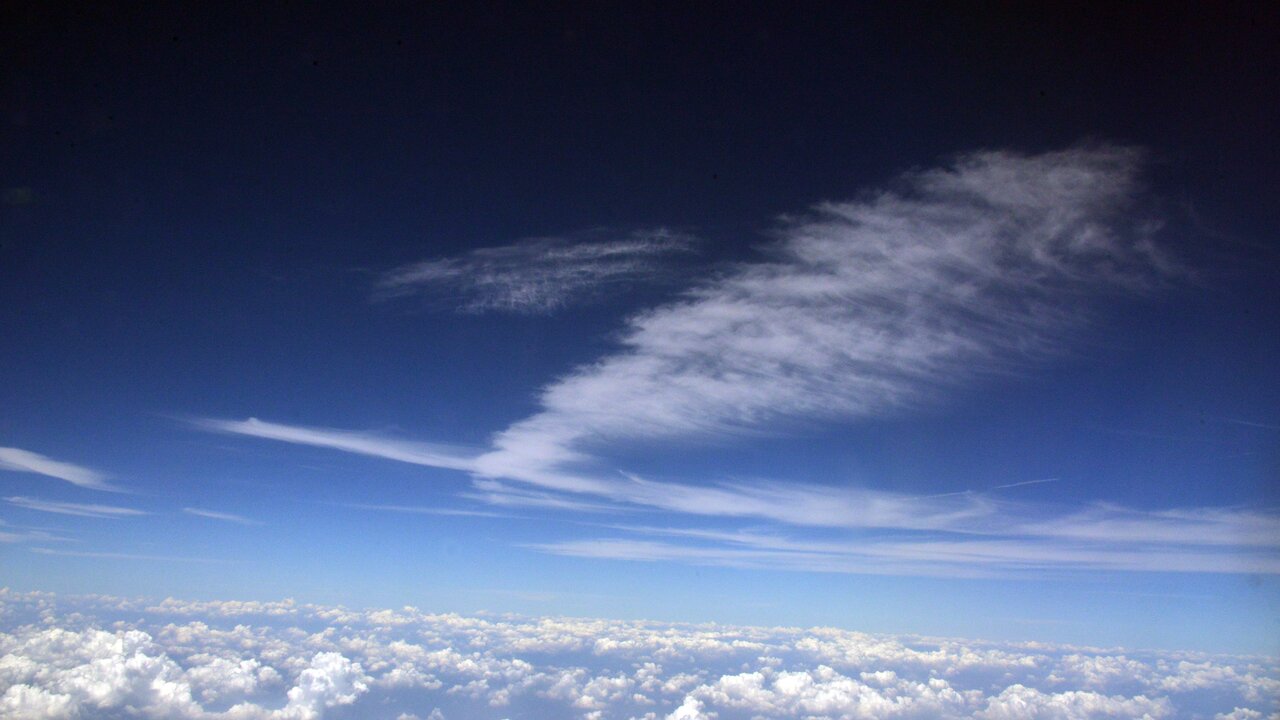 Ein klarer blauer Himmel mit verschiedenen Wolkenformationen. Einige Wolken sind dünn und streifenförmig, während andere fluffig und kumuliform sind, die den Eindruck von Weite und Frieden vermitteln.