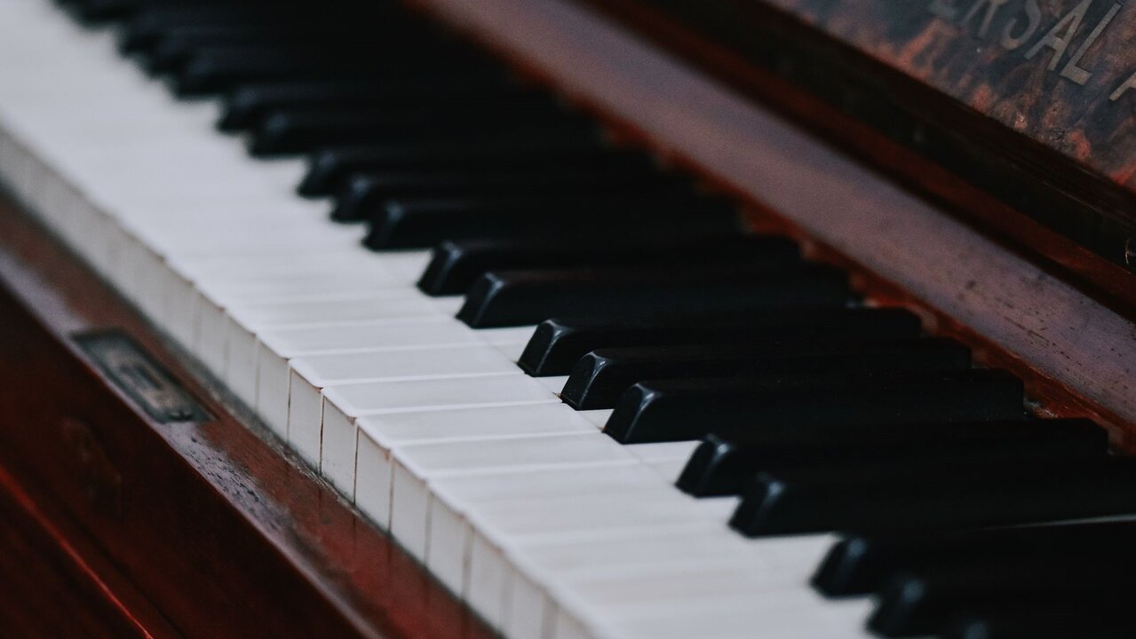 Nahaufnahme von Klaviertasten, die aus weißen und schwarzen Tasten bestehen. Die Holzoberfläche des Klaviers ist sichtbar und verleiht dem Bild eine warme Atmosphäre. Das Bild vermittelt eine musikalische Stimmung und lädt zur Interaktion mit dem Instrument ein.
