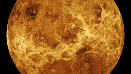 Die Darstellung zeigt den Planeten Venus, der von einer dichten, gelb-orangefarbenen Atmosphäre umgeben ist. Die Oberfläche ist von felsigen und vulkanischen Merkmalen geprägt, die durch Wolken aus Schwefelsäure verborgen sind. Die dunkelsten Stellen deuten auf unterschiedliche geologische Strukturen hin.