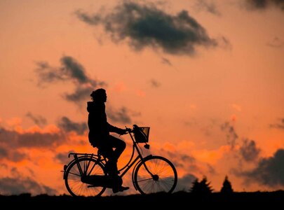 Silhouette einer Person auf einem Fahrrad vor einem bunten Sonnenuntergang. Wolken sind im Hintergrund zu erkennen, während die Umgebung in Dunkelheit gehüllt ist. Die Szene vermittelt ein Gefühl von Ruhe und Freiheit.