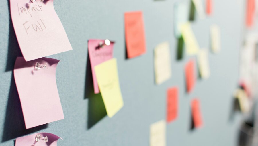 Eine Wand mit bunten Haftnotizen in verschiedenen Farben. Einige Notizen sind beschriftet, während andere leer sind. Die Haftnotizen sind an einer grauen Oberfläche befestigt und scheinen Ideen oder Informationen zu organisieren.