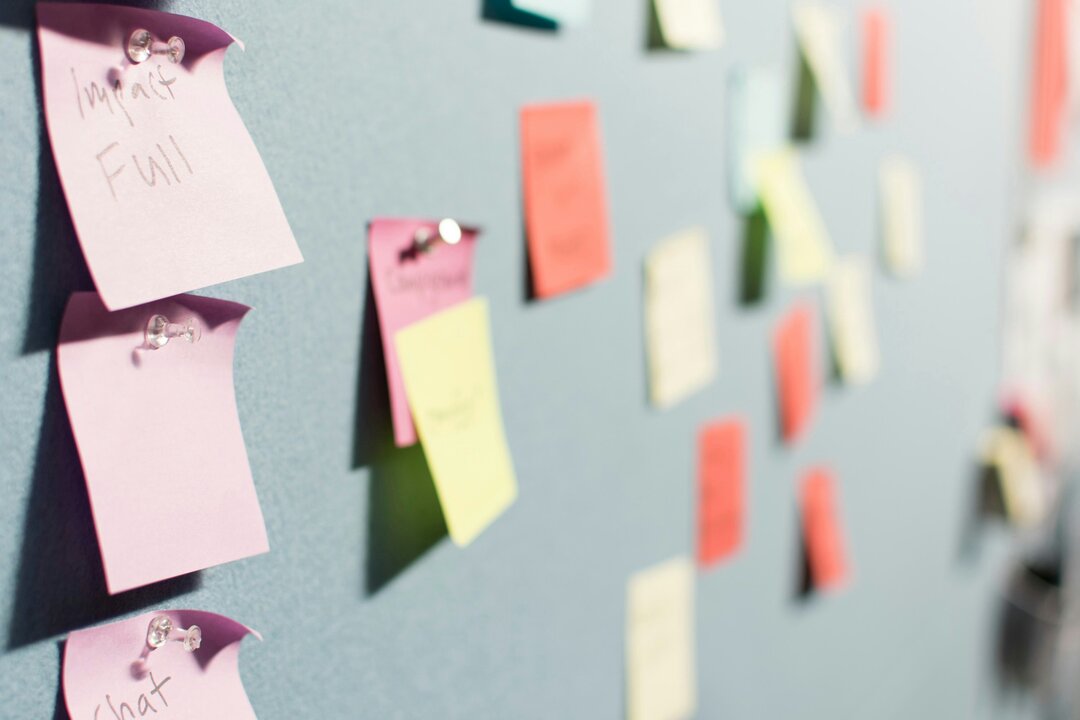 Eine Wand mit bunten Haftnotizen in verschiedenen Farben. Einige Notizen sind beschriftet, während andere leer sind. Die Haftnotizen sind an einer grauen Oberfläche befestigt und scheinen Ideen oder Informationen zu organisieren.