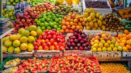 Ein farbenfrohes Obststand mit einer Vielzahl von Früchten. Darunter befinden sich Äpfel, Birnen, Mangos, Trauben, Kiwis, Erdbeeren und Orangen. Die Früchte sind ordentlich in Kisten angeordnet und bilden ein einladendes Bild von Frische und Vielfalt.