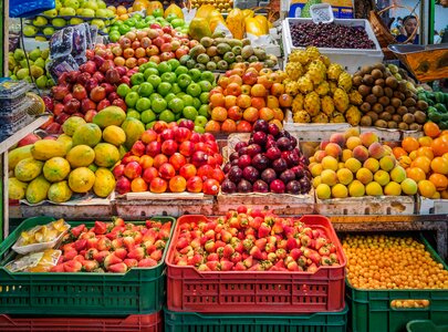 Ein farbenfrohes Obststand mit einer Vielzahl von Früchten. Darunter befinden sich Äpfel, Birnen, Mangos, Trauben, Kiwis, Erdbeeren und Orangen. Die Früchte sind ordentlich in Kisten angeordnet und bilden ein einladendes Bild von Frische und Vielfalt.