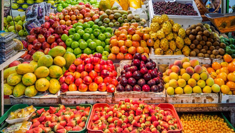 Ein farbenfrohes Obststand mit einer Vielzahl von Früchten. Darunter befinden sich Äpfel, Birnen, Mangos, Trauben, Kiwis, Erdbeeren und Orangen. Die Früchte sind ordentlich in Kisten angeordnet und bilden ein einladendes Bild von Frische und Vielfalt.
