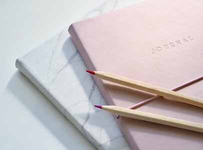 Zwei Journals liegen übereinander, eines in marblemuster und eines in sanftem Rosa. Auf dem rosa Journal sind zwei Bleistifte mit roten und lila Spitzen platziert.