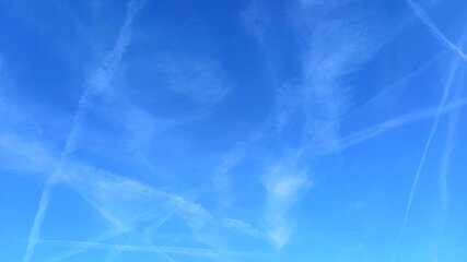 Ein klarer blauer Himmel mit vielen Kondensstreifen, die in verschiedenen Richtungen verlaufen. Die Streifen erzeugen ein lebhaftes Muster, das den Himmel belebt. Der Fokus liegt auf der Himmelsansicht ohne weitere Objekte im Bild.