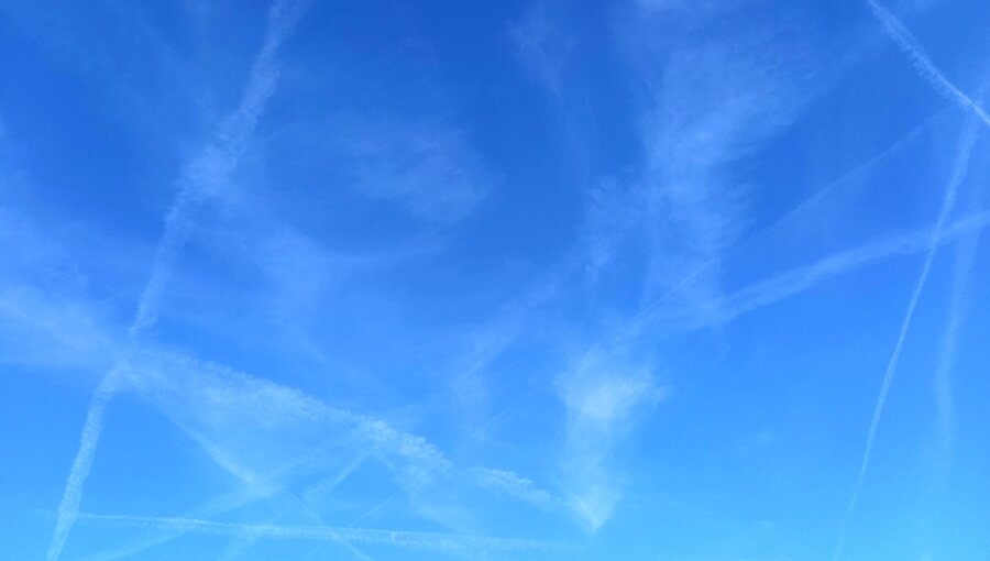 Ein klarer blauer Himmel mit vielen Kondensstreifen, die in verschiedenen Richtungen verlaufen. Die Streifen erzeugen ein lebhaftes Muster, das den Himmel belebt. Der Fokus liegt auf der Himmelsansicht ohne weitere Objekte im Bild.