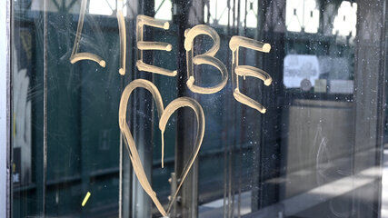Auf einer Glasoberfläche steht in orangefarbenem Schriftzug das Wort "LIEBE", kombiniert mit einem gezeichneten Herz. Die Schrift wirkt handgemalt und ist deutlich sichtbar.