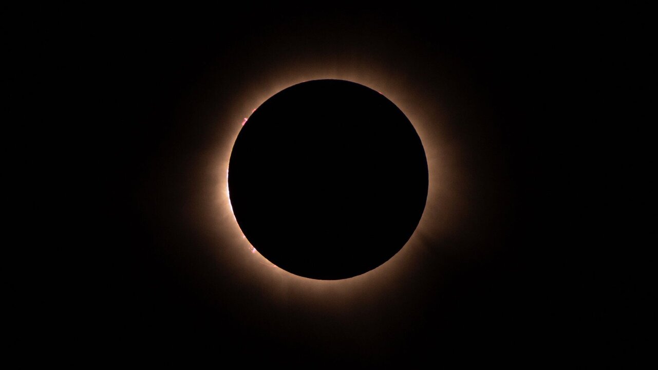 Ein perfekter Ring aus Licht umgibt eine dunkle, runde Scheibe, die die Sonne während einer totalen Sonnenfinsternis verdeckt. Der Hintergrund ist tiefschwarz, was den Kontrast zwischen dem Lichtkreis und der Sonne verstärkt.