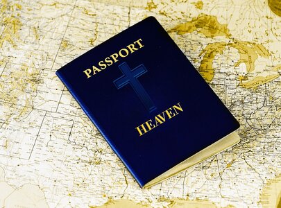 Ein blauer Reisepass mit dem Titel "PASSPORT HEAVEN" und einem Kreuz auf der Vorderseite liegt auf einer alten Weltkarte. Der Reisepass symbolisiert den Glauben und die Vorstellung von einem himmlischen Ziel.