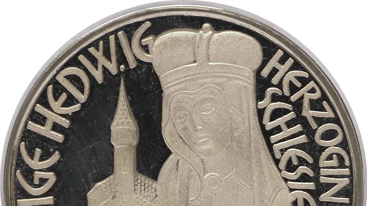 Die Medaille zeigt die Heilige Hedwig, Herzogin von Schlesien, in einem detailreichen Relief. Sie hält ein Buch in den Händen, während im Hintergrund eine stilisierte Kirche zu sehen ist. Umrandet wird das Bild von ihrem Namen und Titel in geschwungenen Buchstaben.